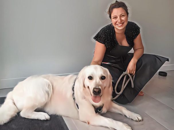 Femme souriante s'accroupissant à côté d'un chien labrador sur un sol intérieur.